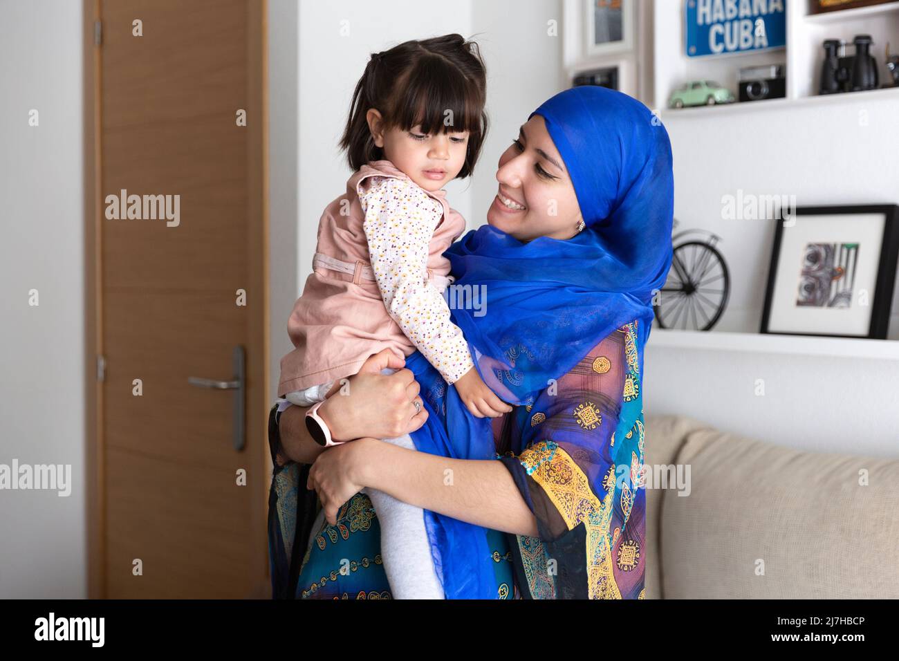 Junge muslimische Frau mit ihrer Tochter in den Armen. Alleinerziehende Familie zu Hause. Stockfoto