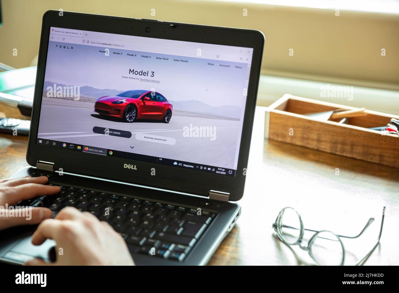 Griechenland, Athen, Januar 23 2022. TESLA FAHRZEUGAUSWAHL. Ad, online rot Tesla Modell 3 Elektro-Auto. PC auf dem Tisch, Hand auf der Tastatur Stockfoto