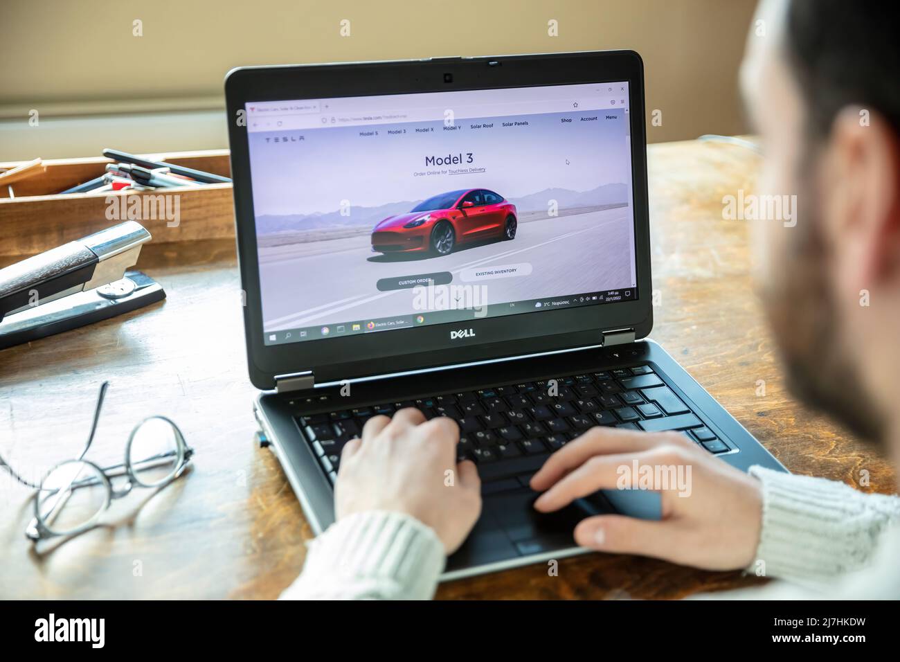 Griechenland, Athen, Januar 23 2022. TESLA FAHRZEUGAUSWAHL. Ad, online rot Tesla Modell 3 Elektro-Auto. PC auf dem Tisch, Hand auf der Tastatur Stockfoto