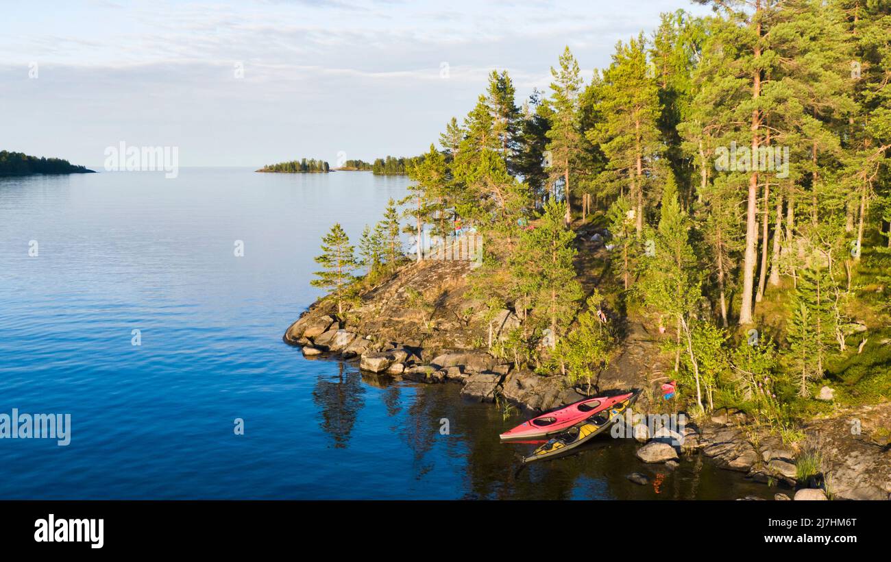 Touristische Kajaks stehen an der malerischen Felsküste mit einem Pinienwald. Atemberaubende Insel in einem großen See an einem warmen Sommerabend. Luftaufnahme. Stockfoto