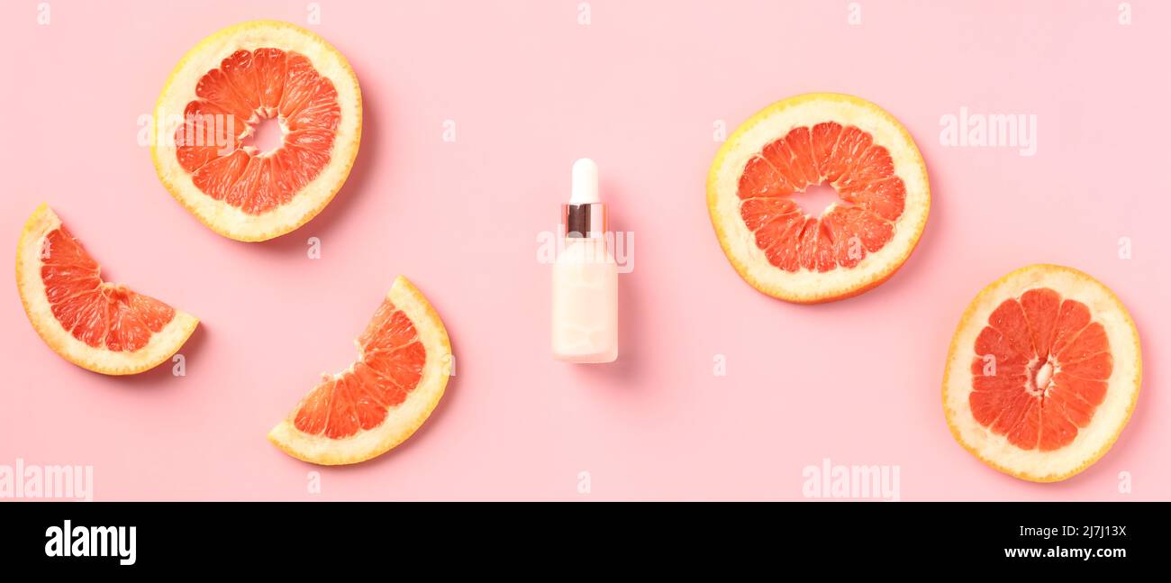 Flasche mit Vitamin-C-Serumextrakt und Grapefruitscheiben auf rosa Hintergrund. Flach liegend. Stockfoto