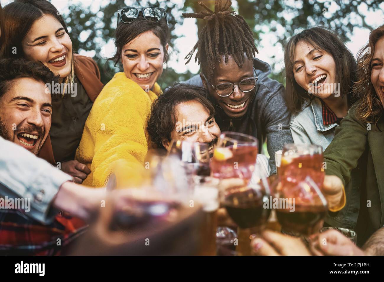 Multiethnische Gruppe von begeisterten jungen Menschen, die gemeinsam Wein und Bier auf der Geburtstagsfeier auf der Terrasse genießen - Lifestyle-Konzept der Multigeneration Stockfoto