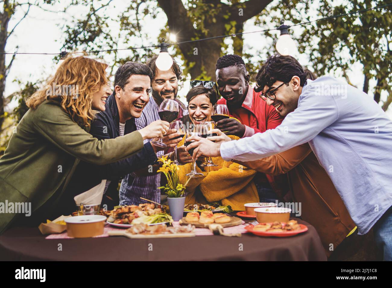 Gesellschaft von fröhlichen Freunden, die Spaß beim Toasten pic nic in Bauernhaus Landschaft - Lifestyle-Konzept mit multigenerationalen glücklichen Freunden Hände bis zu Stockfoto