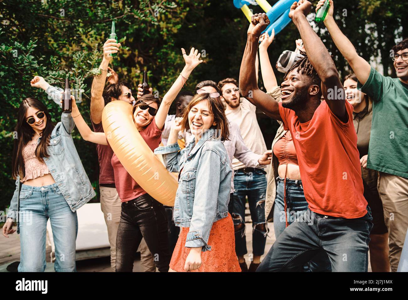 Vielfältige und verspielte Gruppe von jungen Menschen tanzen und Geselligkeit zusammen am Tag Gartenparty - Multigenerational freudige Familie genießen ihr ho Stockfoto