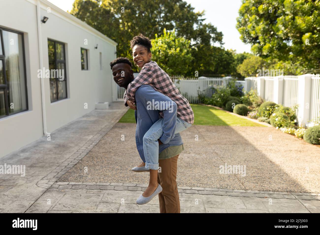 Porträt eines verspielten afroamerikanischen jungen Mannes, der eine junge Freundin huckepack, während sie im Hof steht Stockfoto