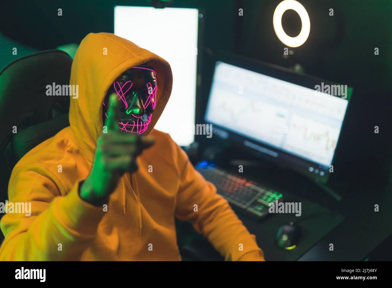 Mann mit einer gruseligen Neonmaske sitzt vor einem Computer-Hacking-Konzept-Medium aus der Nähe. Hochwertige Fotos Stockfoto