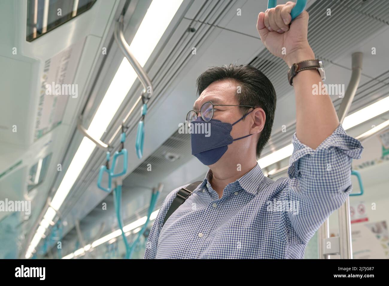 Mann Pendler mit Gesichtsmaske auf halten an Handgriff in einem fahrenden Zug. Maskiertes Transitkonzept. Stockfoto