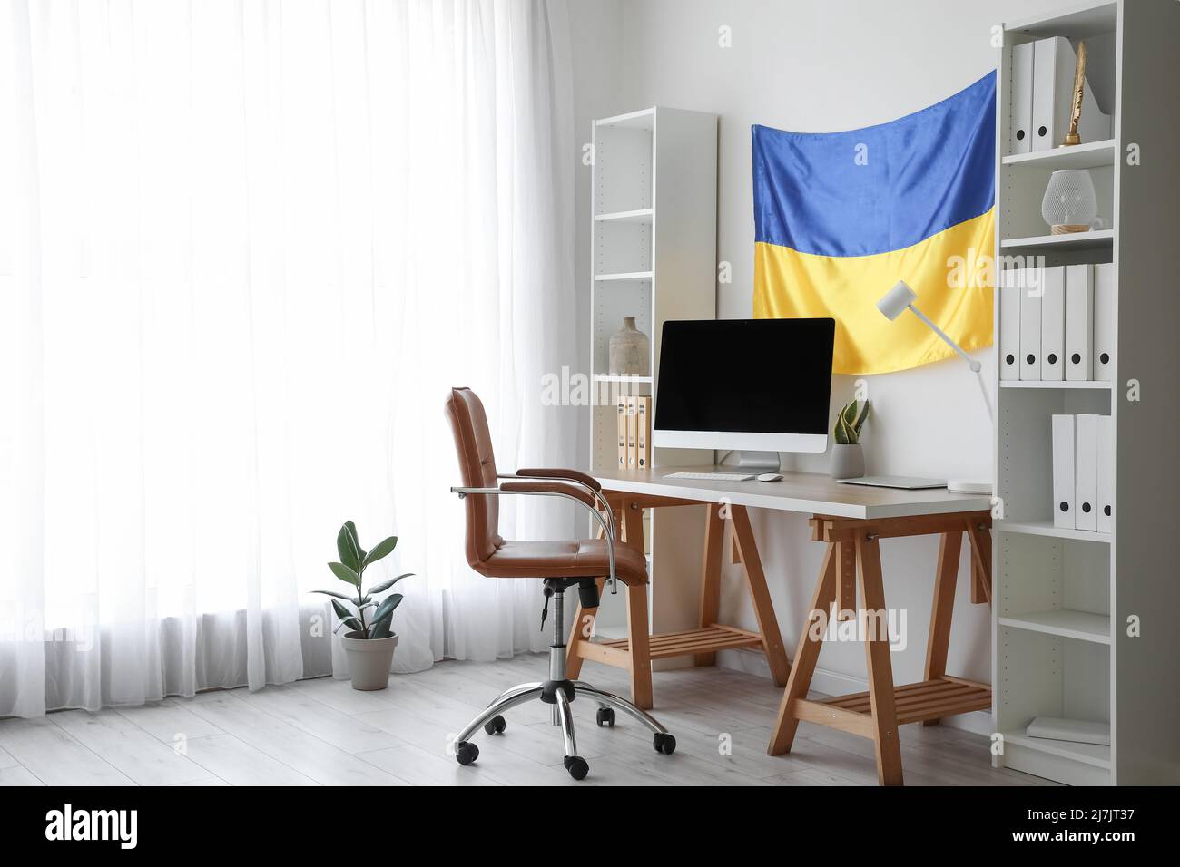 Inneneinrichtung eines modernen Büros mit Arbeitsplatz, Regalen und hängender ukrainischer Flagge Stockfoto