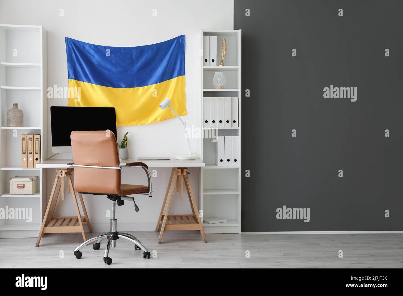 Inneneinrichtung eines modernen Büros mit Arbeitsplatz, Regalen und hängender ukrainischer Flagge Stockfoto