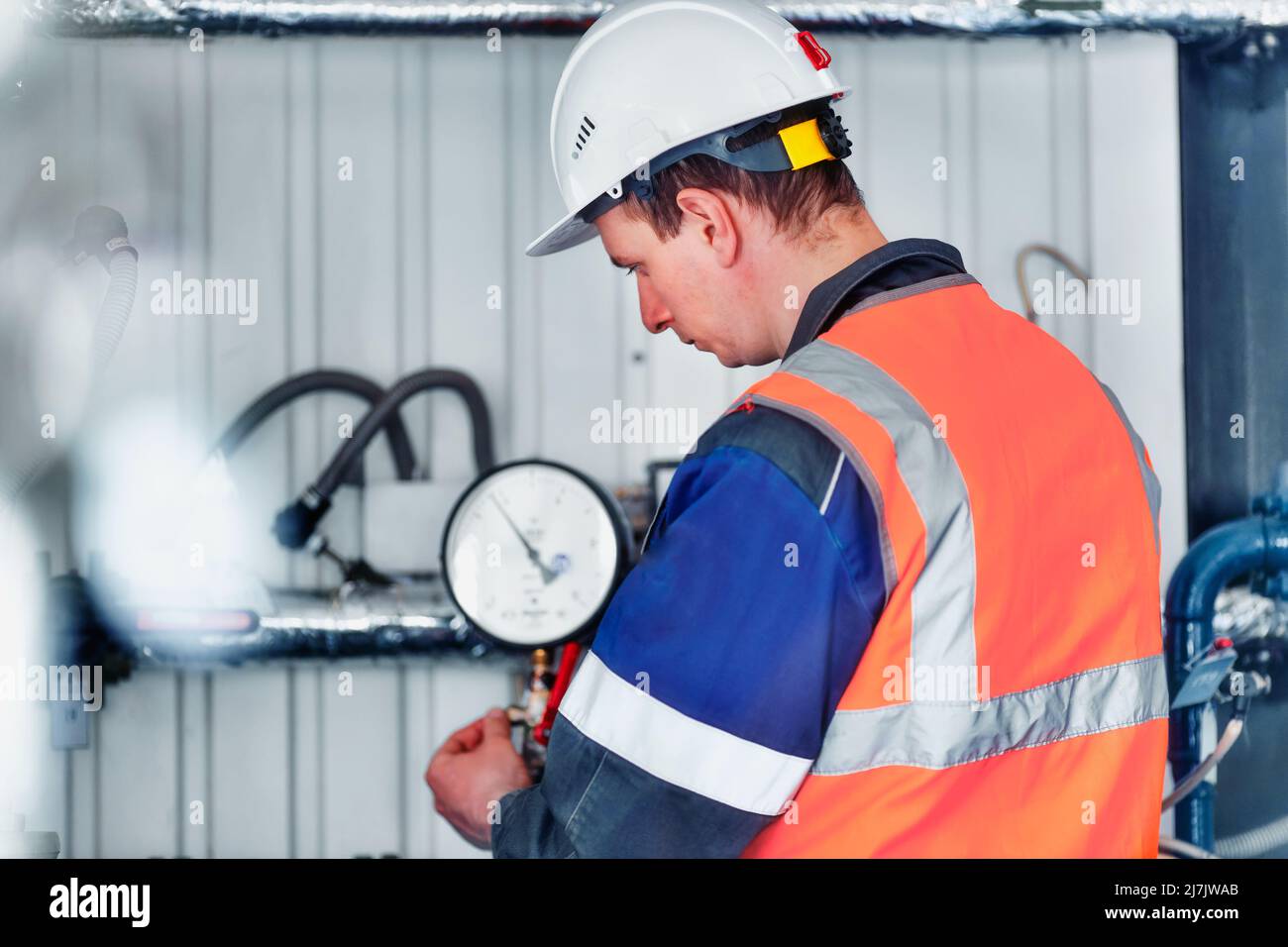 Der Betreiber des Gaskesselhauses in Helm und Schutzweste überprüft die Druckwerte der Druckmessgeräte in der Produktionsanlage. Vorbereitung von Anlagen und Geräten für die Heizperiode. Gasversorgung nach Europa. Stockfoto