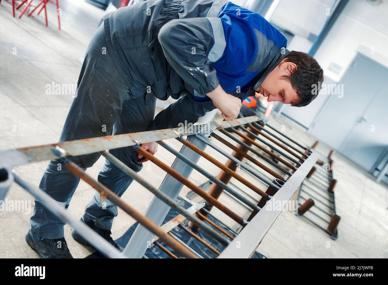 Maler von 30-40 Jahren kaukasischen Aussehen malt Metallstruktur in der Produktionshalle mit Pinsel. Echter Workflow. Stockfoto