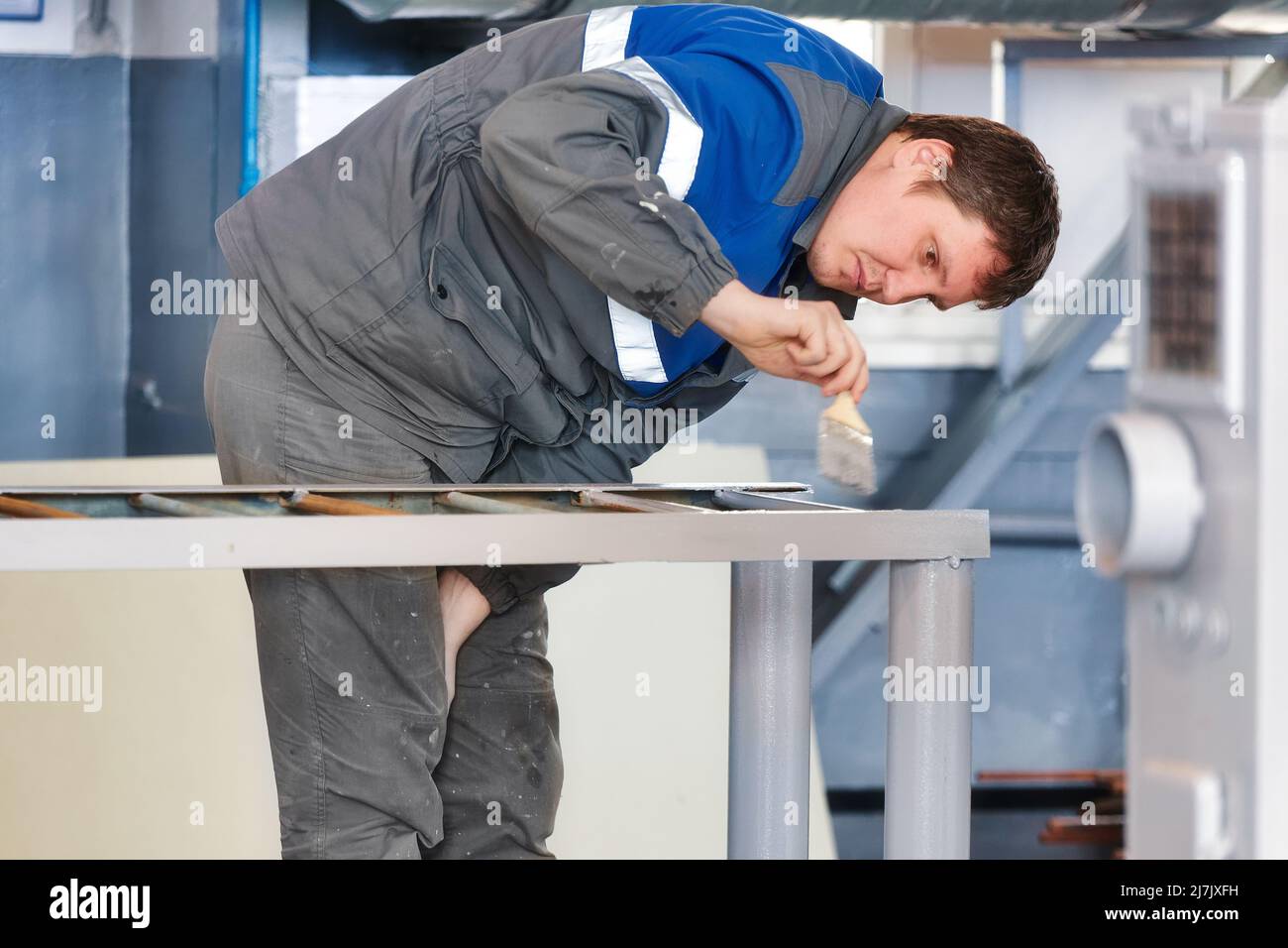 Maler von 30-40 Jahren kaukasischen Aussehen malt Metallstruktur in der Produktionshalle mit Pinsel. Echter Workflow. Stockfoto