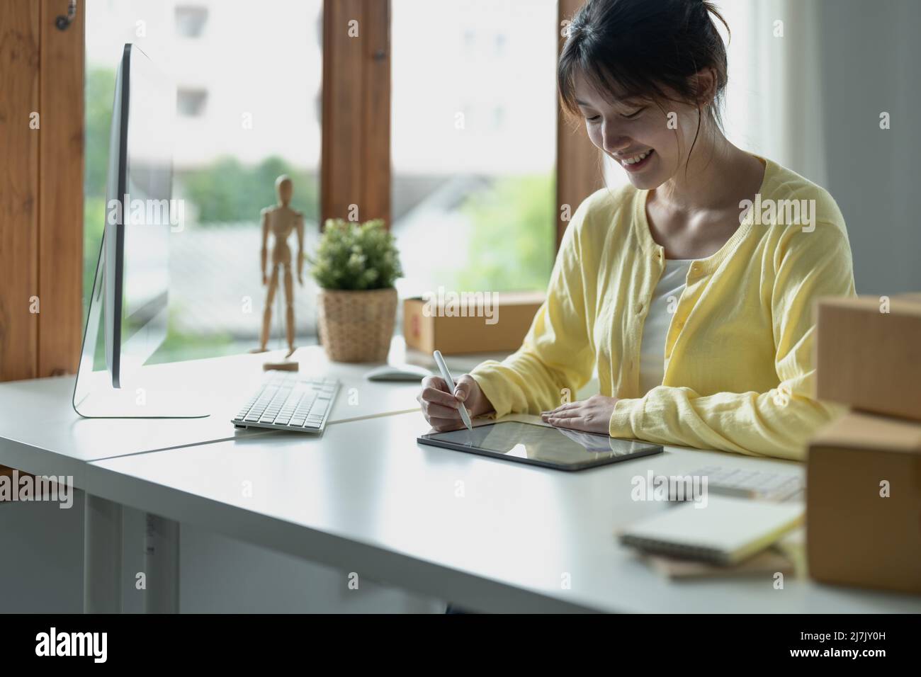 Junge asiatische kreative Designer halten Stift Zeichnung auf dem Bildschirm des digitalen Tabletts, während im modernen Büro sitzen. Stockfoto