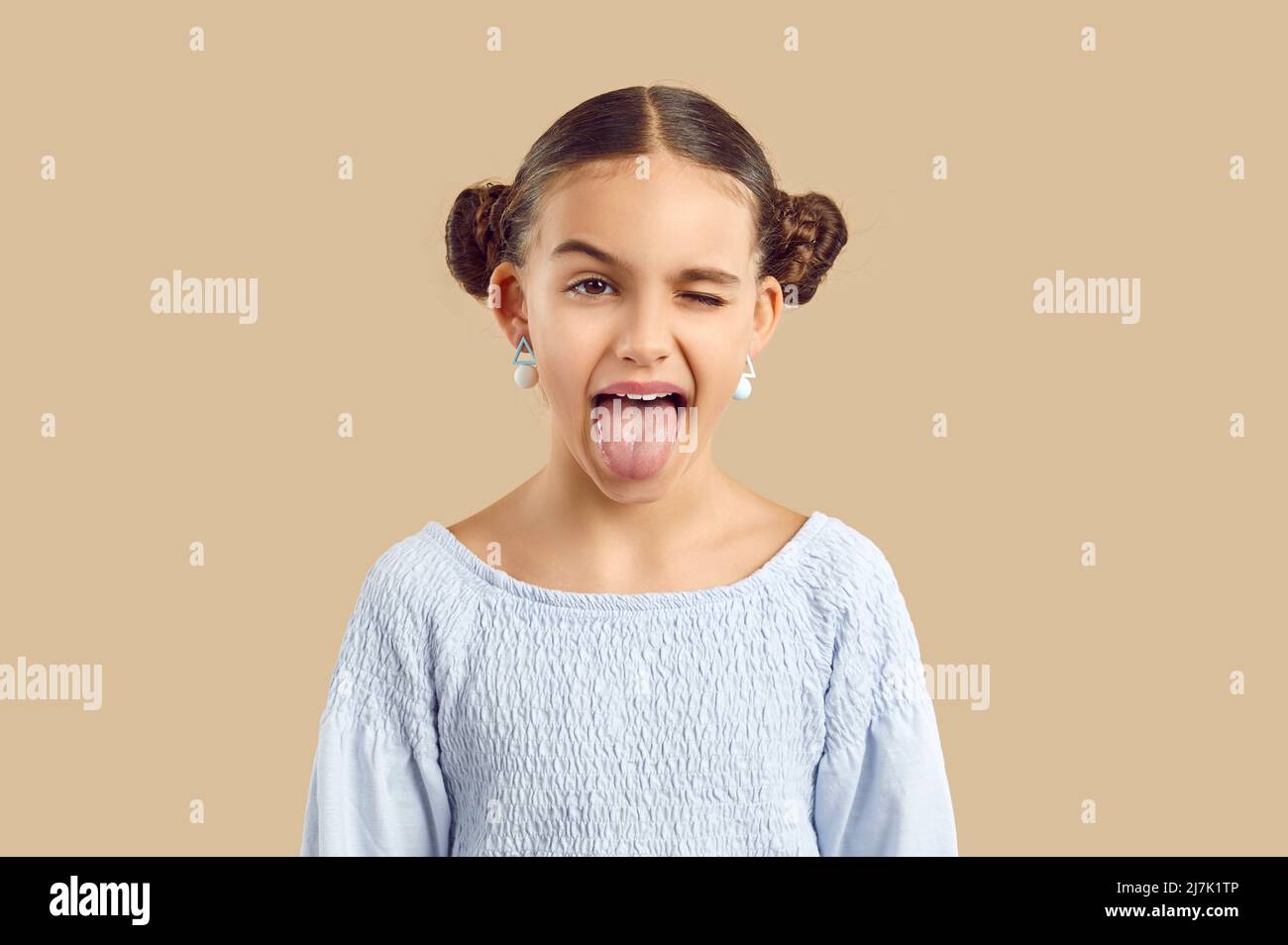 Studioaufnahme eines lustigen, frechen kleinen Mädchens, das ihre Zunge herausstreckt und ihr Auge winkend macht Stockfoto