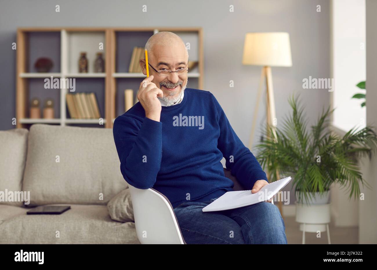 Porträt eines positiven älteren Mannes, der gerne zu Hause Ideen in sein Notizbuch schreibt. Stockfoto