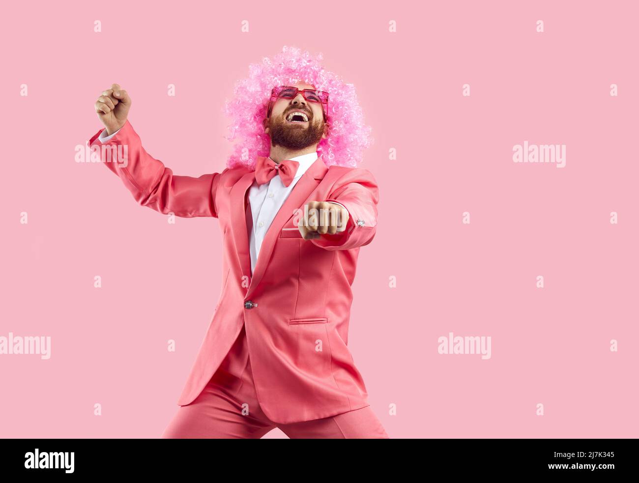 Fröhlicher verrückter Mann in rosa Perücke macht lustige Tanzbewegungen isoliert auf rosa Hintergrund. Stockfoto