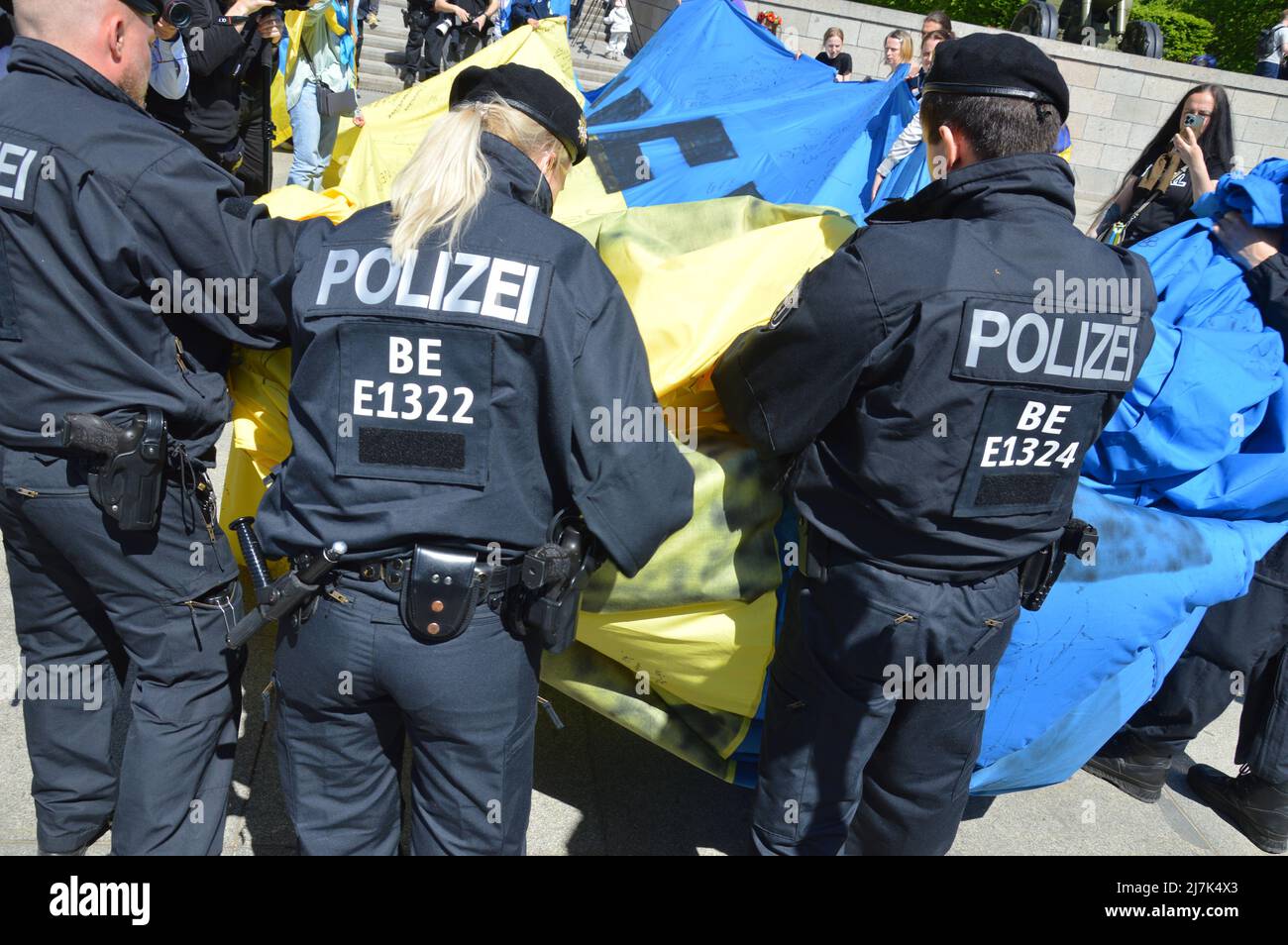 Am 8. Mai 2022 rollt die Polizei eine riesige ukrainische Flagge auf, die von den Demonstranten am sowjetischen Kriegsdenkmal in Tiergarten, im Zentrum von Berlin, gezeigt wird. Stockfoto