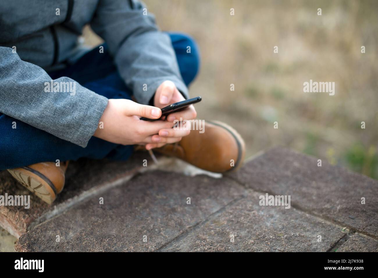 Ein Schuljunge benutzt im Frühjahr in der Natur in der Stadt ein Mobiltelefon in den Händen. Freizeit. Stockfoto