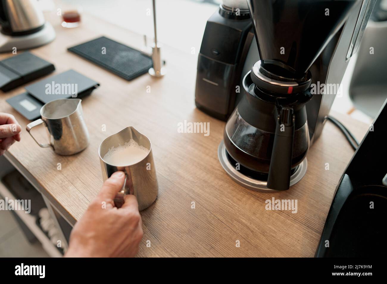 Der Barista schäumte Milch für Latte in einem Stahlkrug Stockfoto