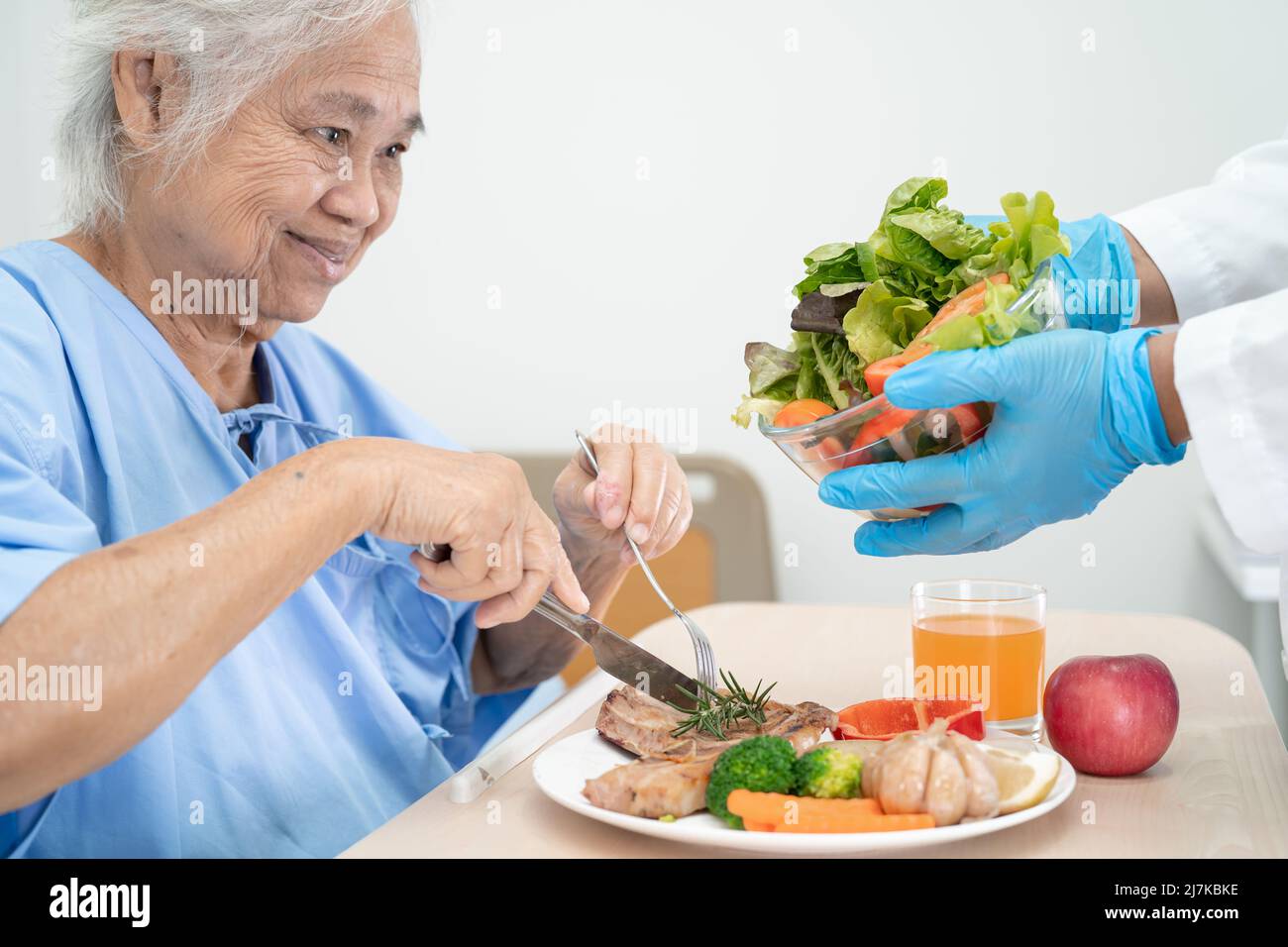 Asiatische ältere oder ältere alte Dame Frau Patientin essen Frühstück und Gemüse gesunde Lebensmittel mit Hoffnung und glücklich, während sitzen und hungrig auf dem Bett in der Zusammenarbeit Stockfoto