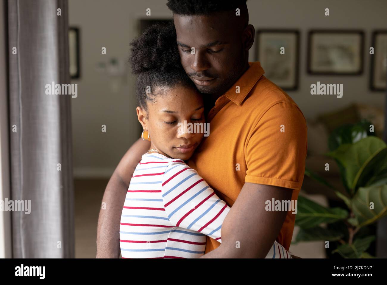 afroamerikanischer junger Freund und Freundin mit geschlossenen Augen umarmt, während sie zu Hause stehen Stockfoto