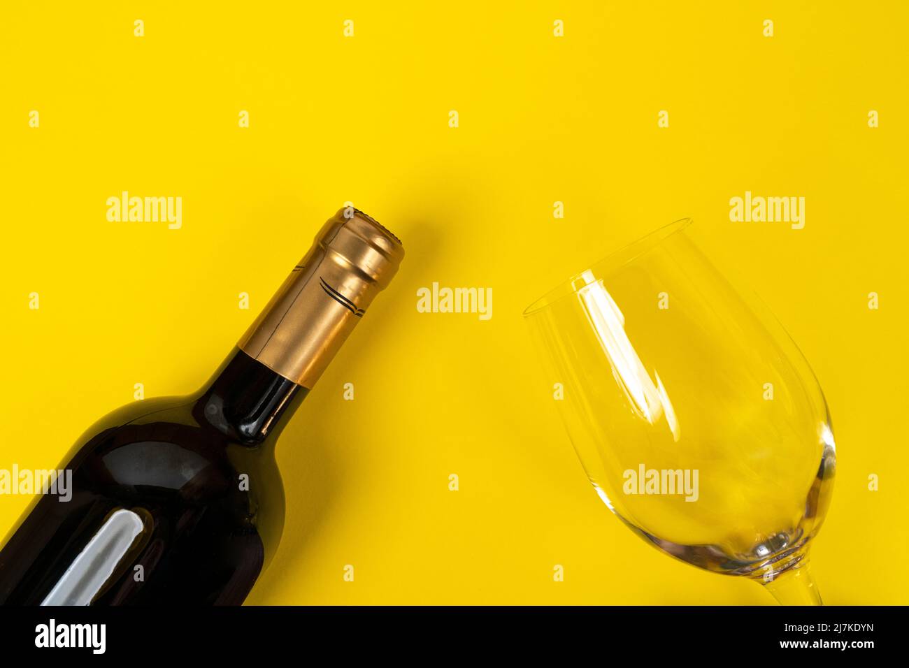Eine Flasche Rotwein und ein Glas auf einer gelben Oberfläche Stockfoto