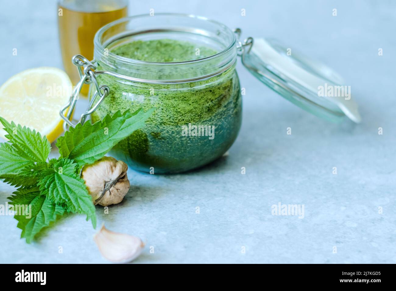 Vegetarische Brennnessel, Knoblauch, Olivenöl, Zitrone und Walnuss. Offenes Glas mit hausgemachtem Brennnesselpesto auf grauem Hintergrund. Veganes Brennnesselpesto Stockfoto