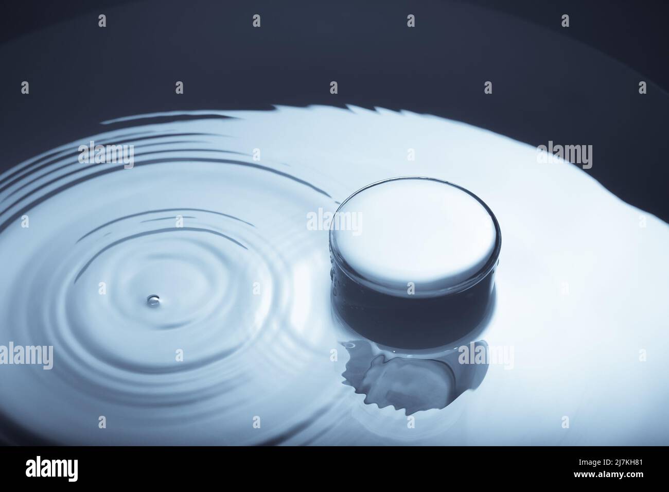 Minimalistisches Bild eines Glases Wasser mit Tropfen auf die Wasseroberfläche. Abstraktes Bild von Wasser in blauem Monochrom. Stockfoto