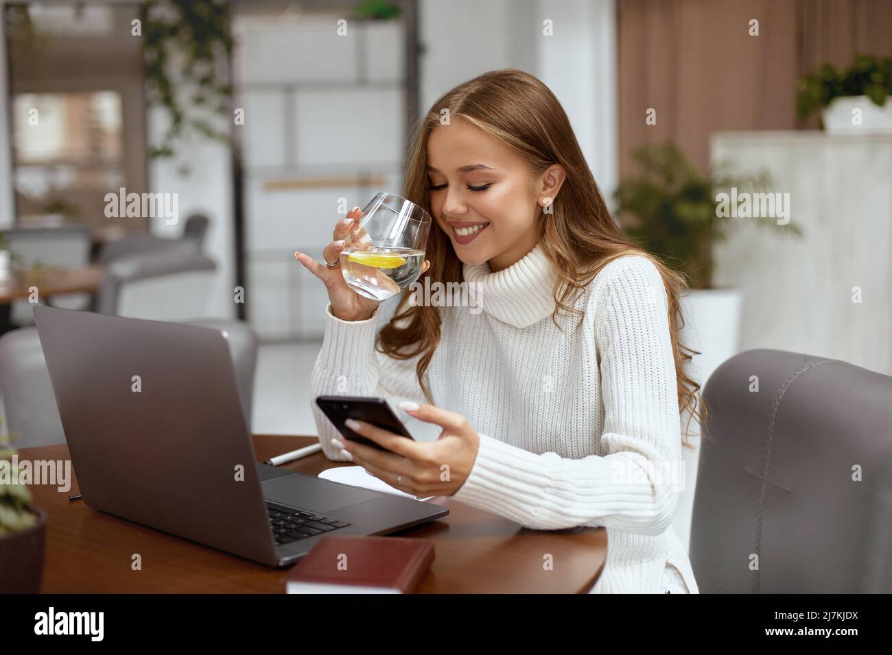 Schöne Frau, die im Büro am Tisch sitzt und Wasser trinkt Stockfoto