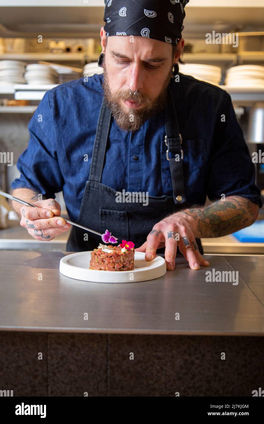 Gebärtete Chefköchin auf der Schürze, die frischen, leckeren Rindertartar auf dem Teller in der Küche des Restaurants verschönert Stockfoto