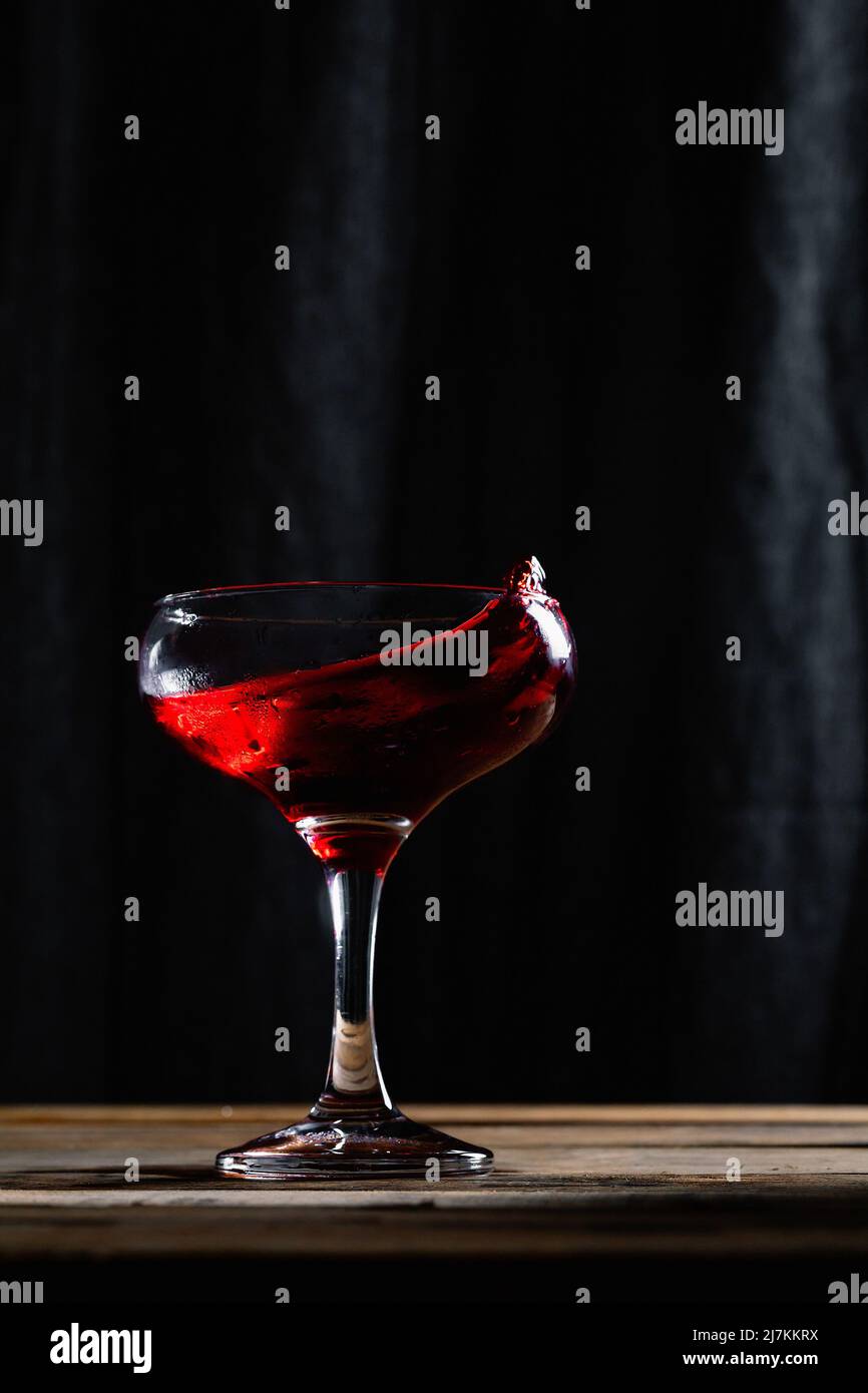 Spritzt leckeren alkoholischen Rotwein mit kleinen Tropfen in transparentem Weinglas auf Tisch vor schwarzem Hintergrund in modernen Studio platziert Stockfoto