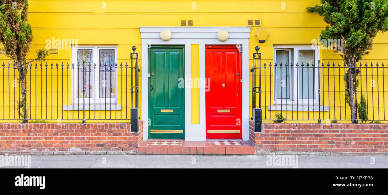 Fassade eines gelben Wohnhauses mit Fenstern und bunten Türen in der Nähe von Metallzaun und Gehweg auf der Straße der Stadt Stockfoto