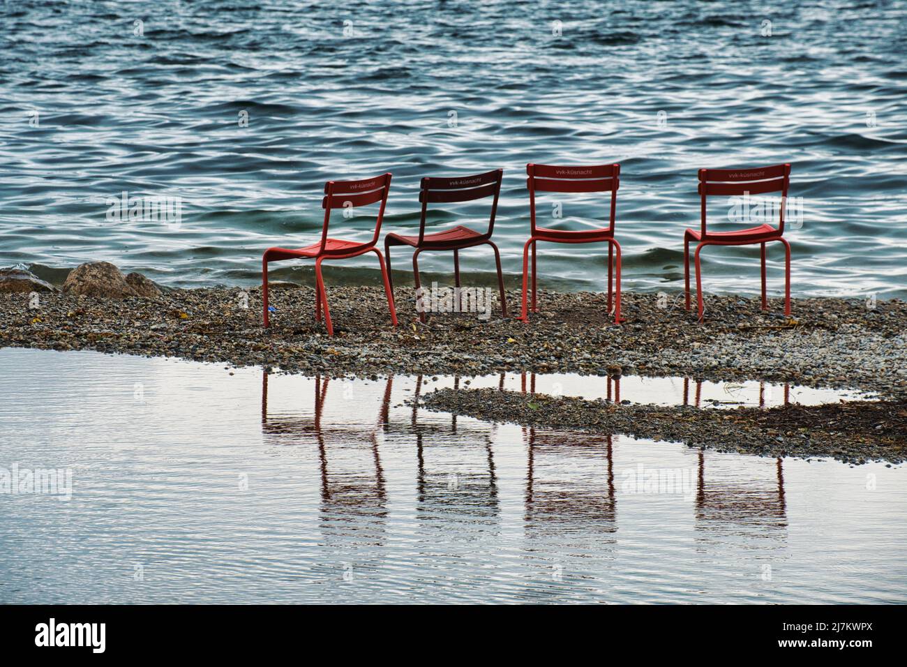 Vier rote Stühle mit Reflexionen am Ufer des Zürichsees, Schweiz Stockfoto