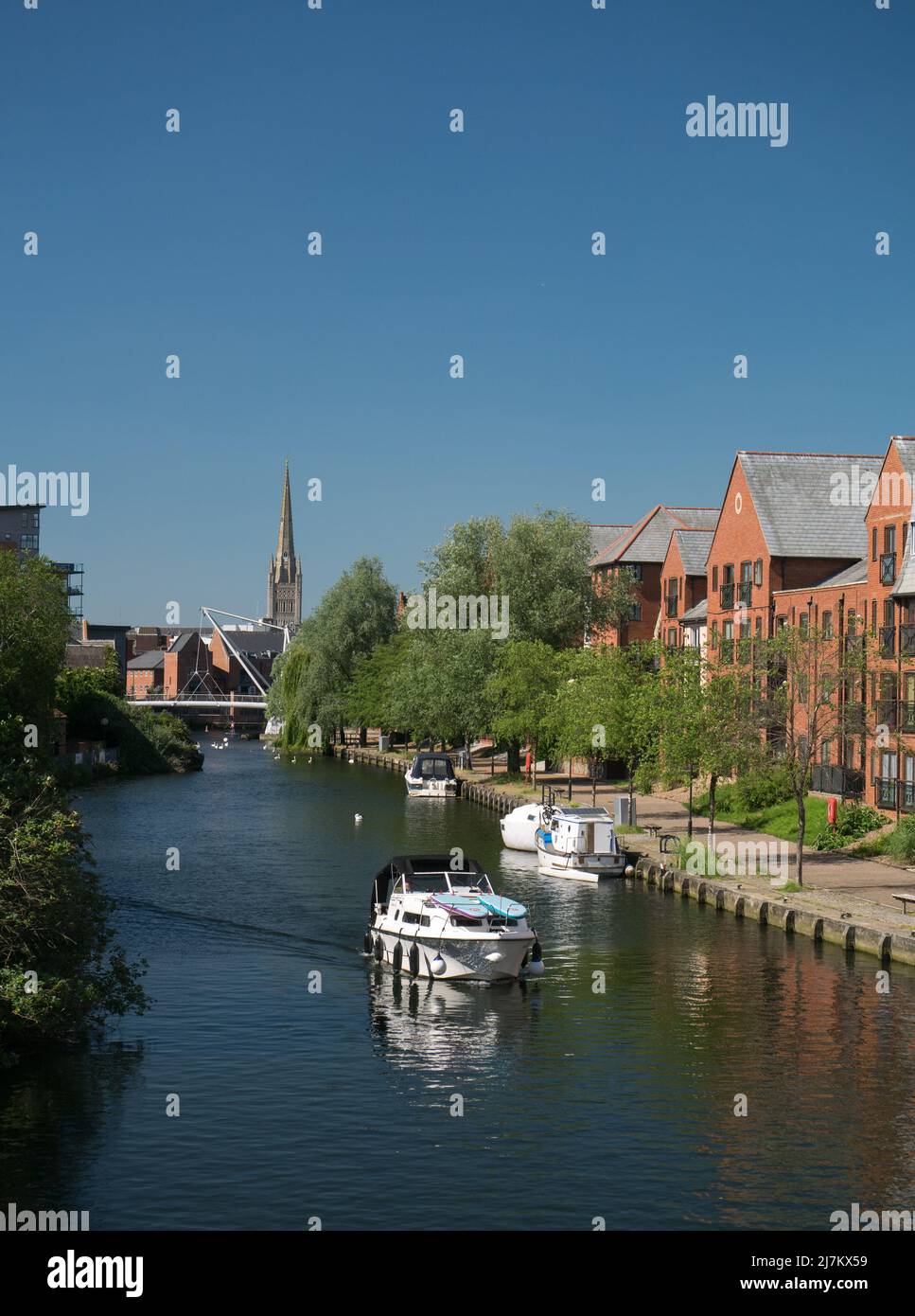 Der Fluss Wensum in der Stadt Norwich, Teil der Norfolk Broads, mit Neuentwicklung & Cathedral Spire, Norwich, Norfolk, England, Großbritannien Stockfoto