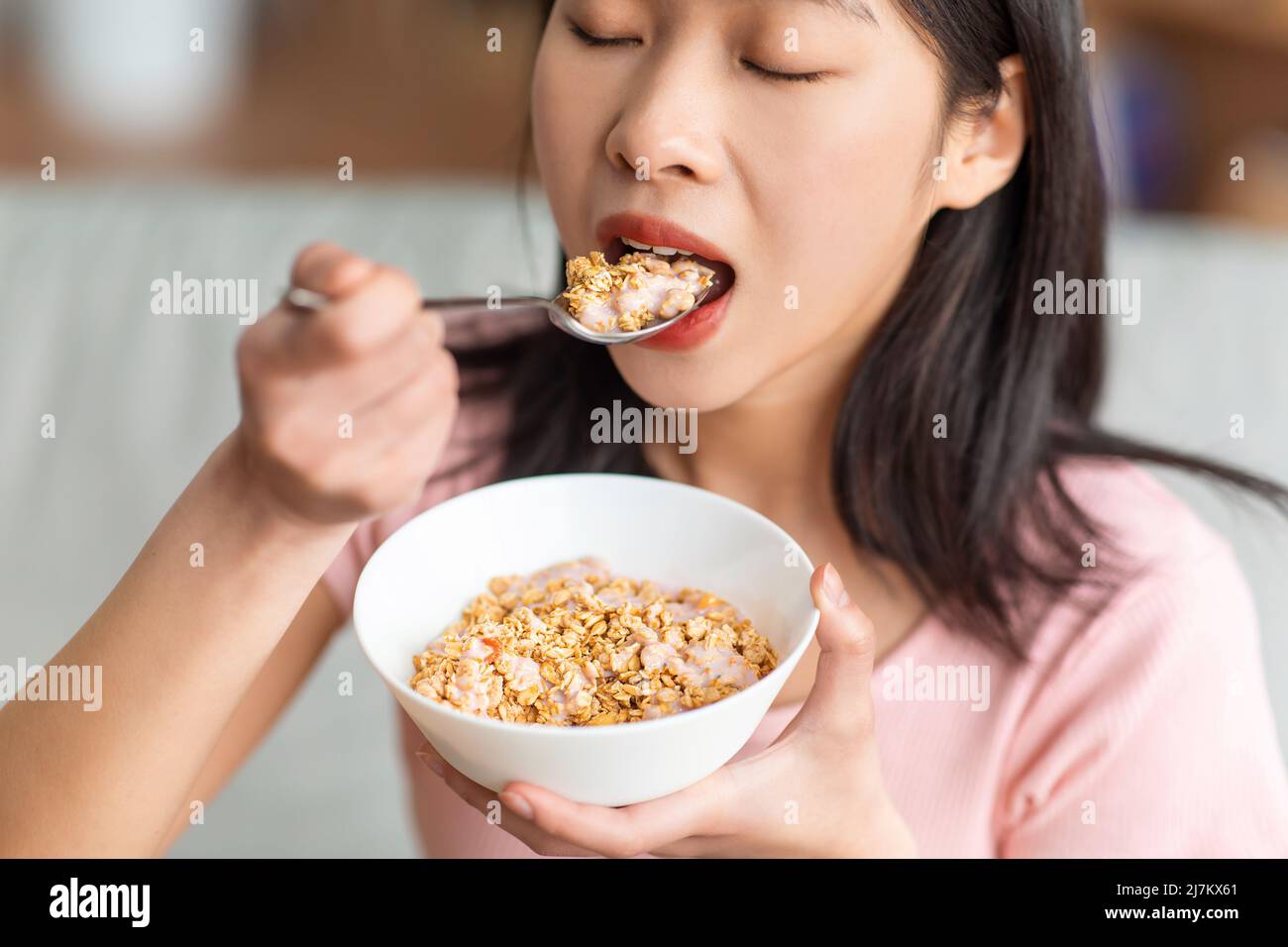 Gesunde Ernährung Konzept. Koreanische Dame, die Müsli mit Joghurt isst, nahrhaftes Frühstück zu Hause, Nahaufnahme Stockfoto