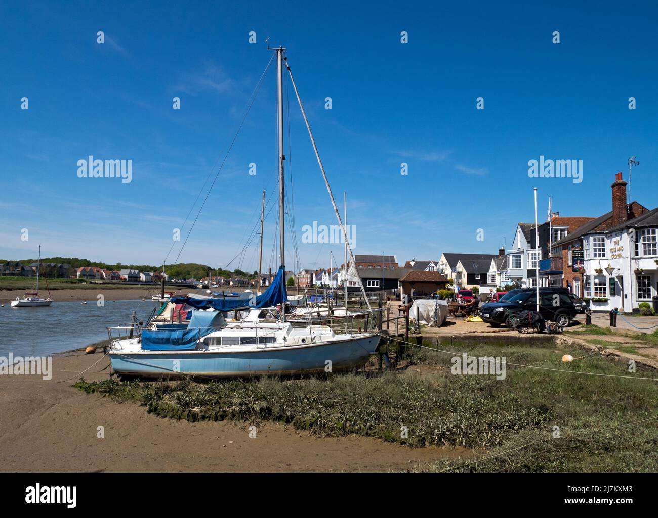 Am Strand vor der Mündung des Flusses Colne festmachen Segelboote zusammen mit dem Gebäude der antiken Stadt Wivenhoe, Essex, England, Großbritannien Stockfoto