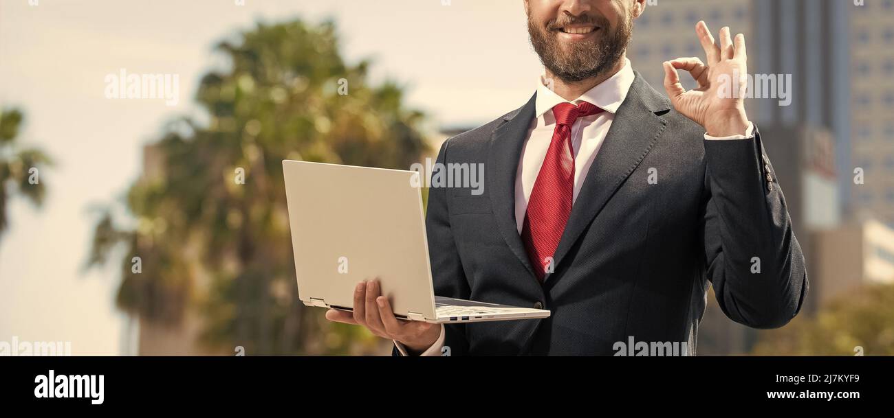 Selbstbewusster Mann in elegantem Anzug mit pc außen zeigen ok Geste, Büroangestellter Stockfoto