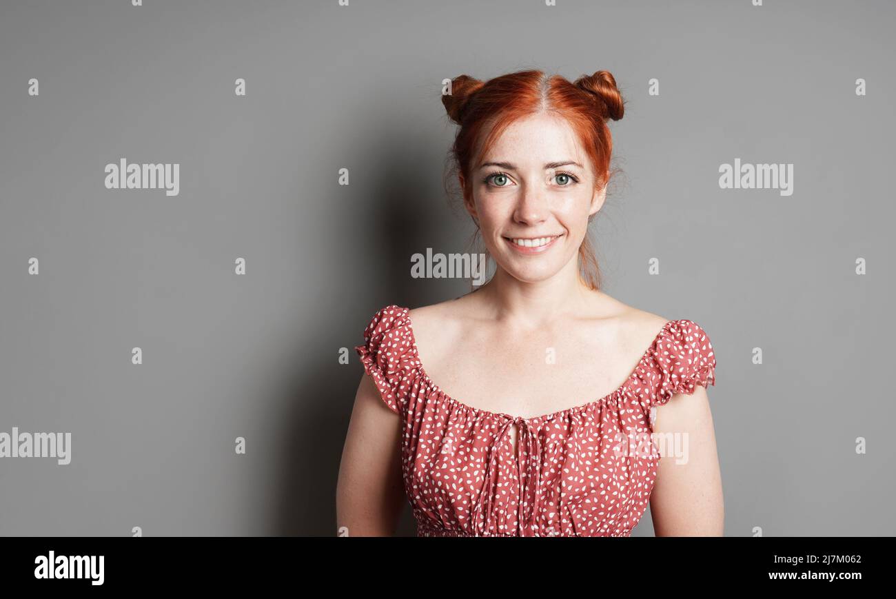 Glückliche junge Frau mit einem großen, toothy Lächeln und roten Haaren Space Buns Stockfoto