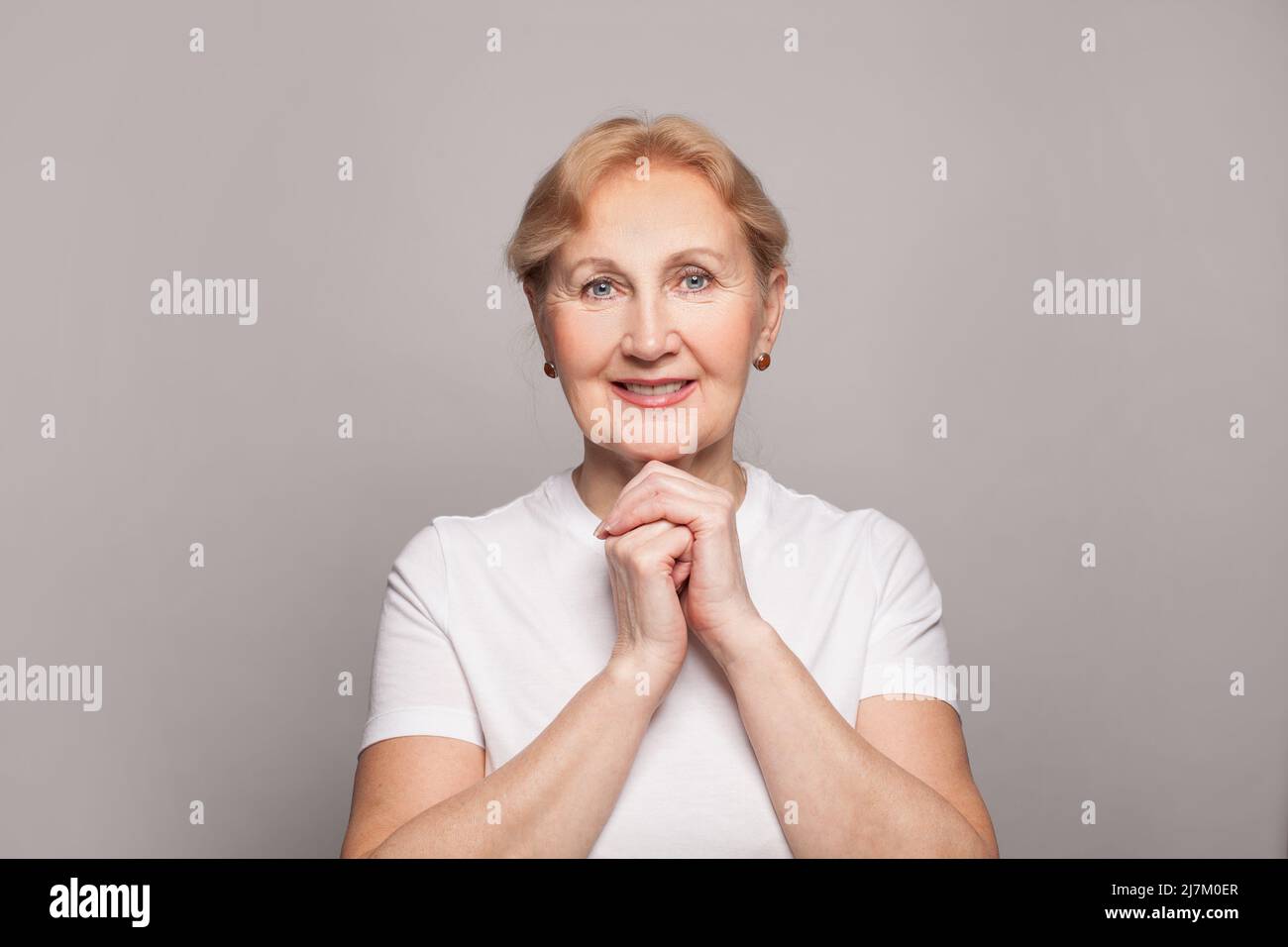 Schöne Frau mittleren Alters lächelt auf grauem Wandhintergrund Stockfoto