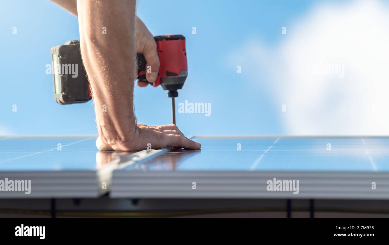 Nicht identifizierter Mann, der Solarzellen mit einem Akkuschrauber auf dem Hausdach installiert. Konzentrieren Sie sich auf die Hand Stockfoto
