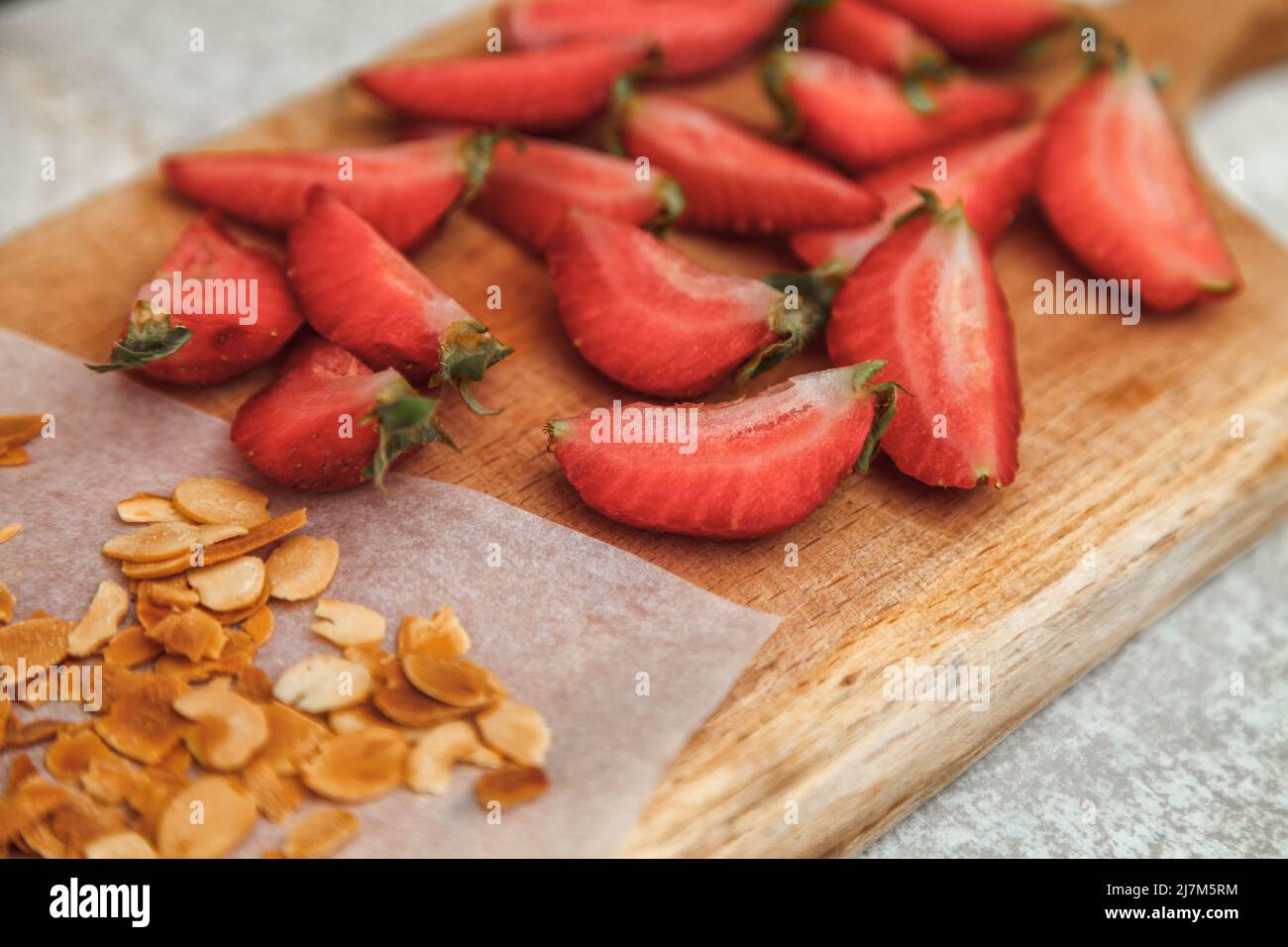 Geschnittene frische Erdbeeren und gebratene Mandelflocken zum Dekorieren und Dekorieren einer Baiser-Rolle Stockfoto