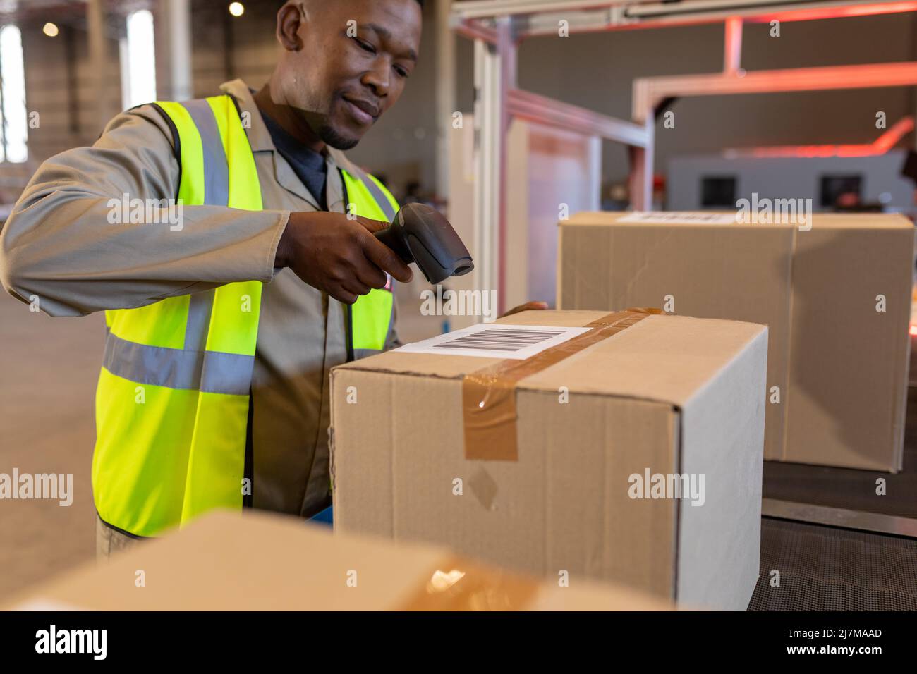afroamerikanischer junger männlicher Lagerarbeiter scannt Barcode mit Lesegerät auf Karton Stockfoto