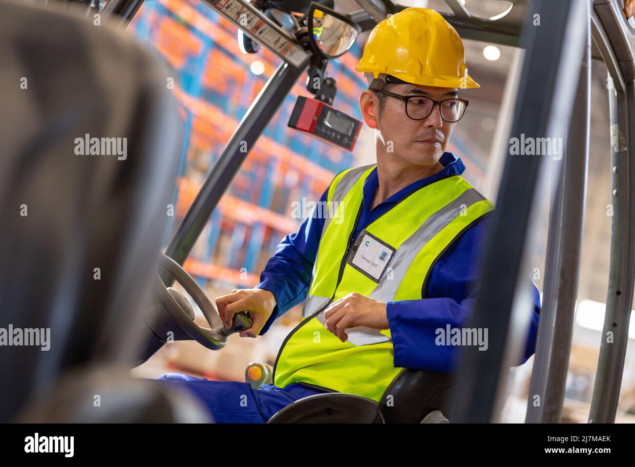 Serious Asian reifen männlichen Arbeiter schaut weg, während im Gabelstapler im Lager sitzen Stockfoto
