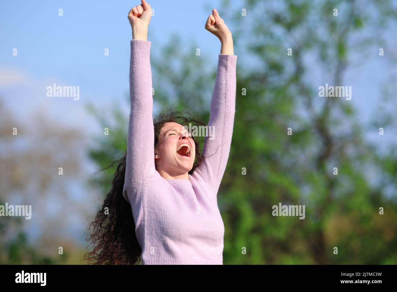 Eine aufgeregte Frau, die in einem Park die Arme hebt und einen guten Tag im Pullover feiert Stockfoto