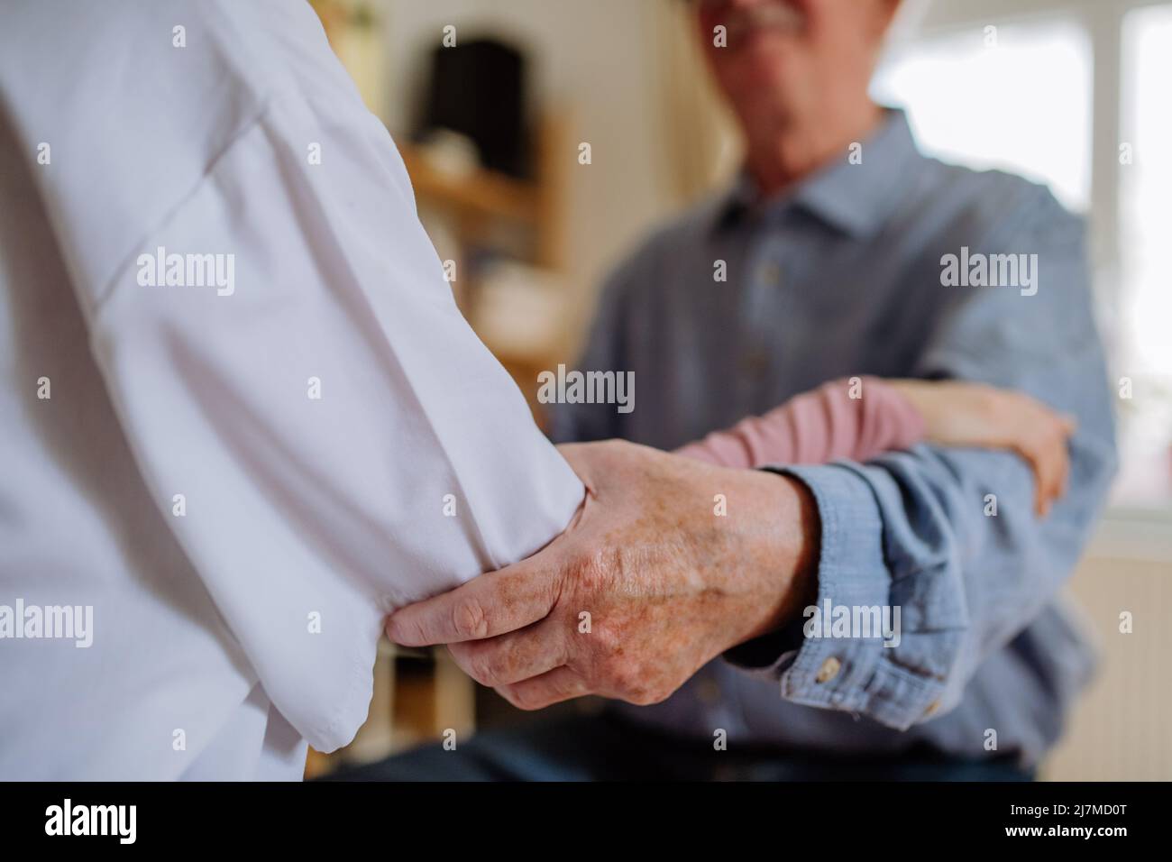 Nahaufnahme eines Arztes, der die Hand eines älteren Patienten hält und ihn während eines Arztbesuchs zu Hause tröstet. Stockfoto