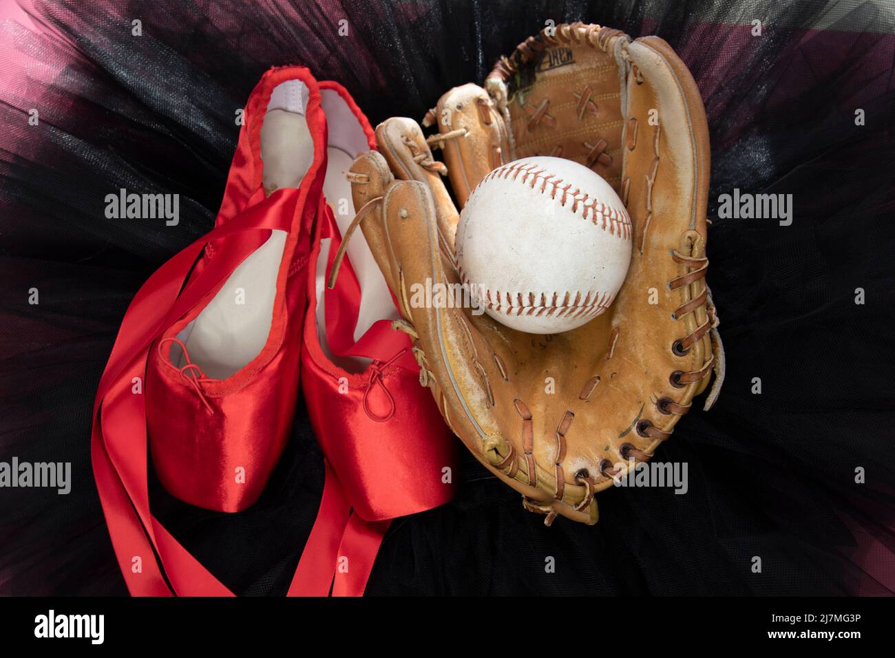 Softball-Handschuh, Ball- und Ballettschuhe auf einem schwarzen Tutu. Stockfoto