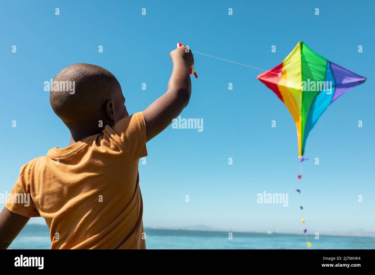 afroamerikanischer Junge genießt Drachen fliegen gegen blauen Himmel an sonnigen Tag Stockfoto