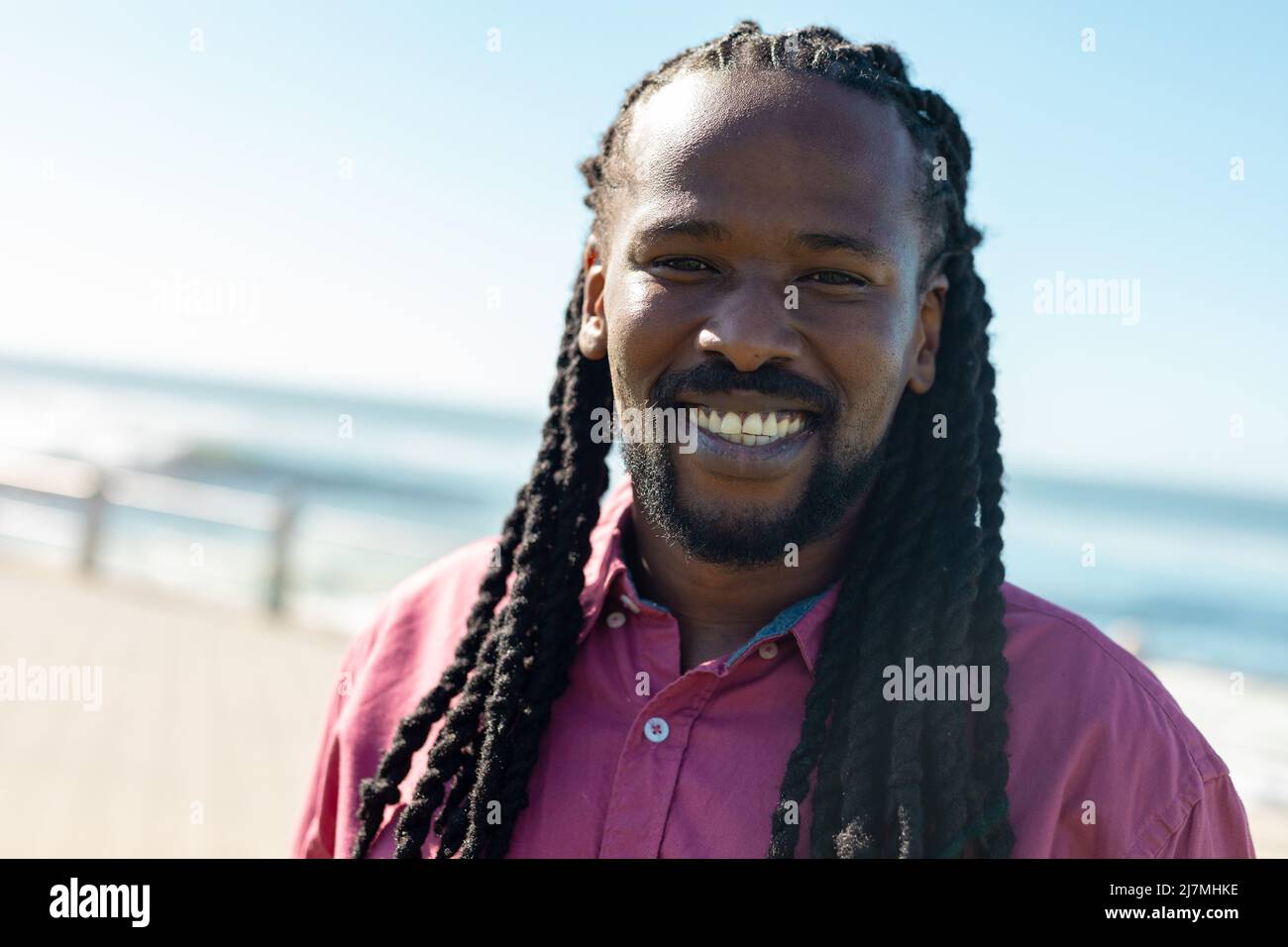 Porträt eines lächelnden afroamerikanischen Mannes mit langen geflochtenen schwarzen Haaren an einem sonnigen Tag Stockfoto