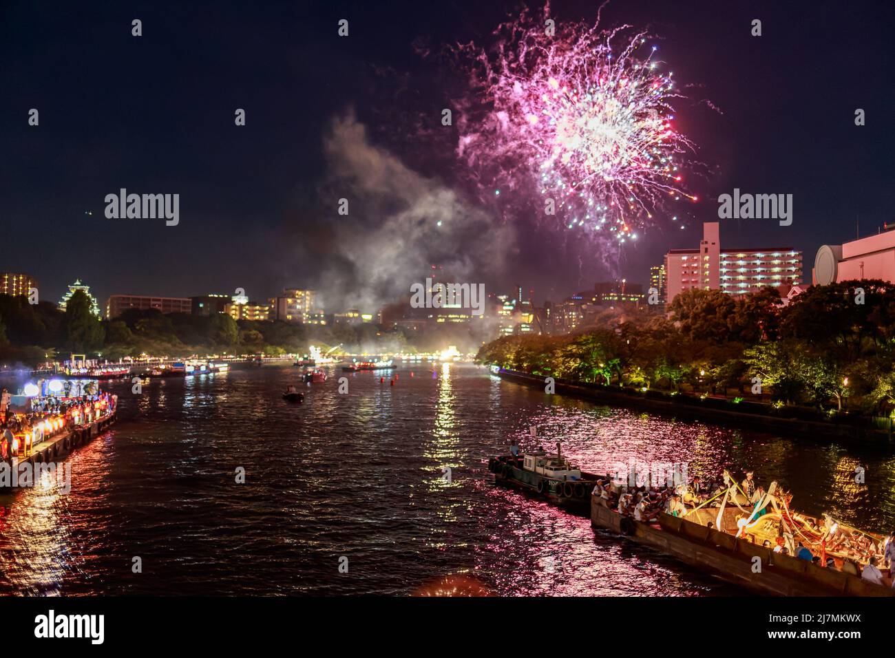 Beim Sommerfest explodieren purpurrote Feuerwerke über dem Flussufer Stockfoto