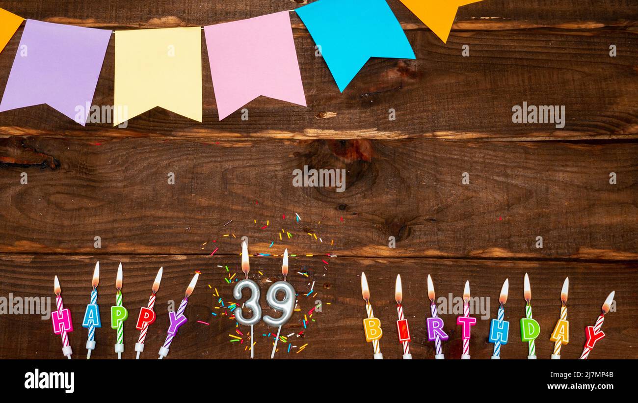 Draufsicht, Geburtstagsdekorationen aus Kerzenbuchstaben mit Feuer und Festtagsgirlanden, Kopierraum. Alles gute zum Geburtstag Hintergrund mit Nummer auf braunem Tisch. Stockfoto